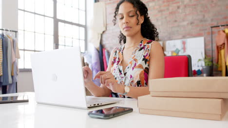 Glückliche-Biracial-Weibliche-Modedesignerin-Mit-Laptop-Und-Smartphone-Im-Studio,-Zeitlupe