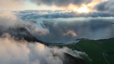 drone ascends above foggy mannen peaks with utakleiv beach and ocean glowing in midnight sun