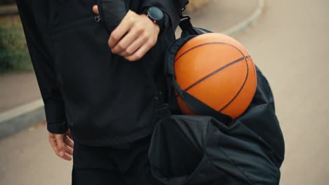 Primer-Plano-De-Un-Hombre-Vestido-De-Negro-Sosteniendo-Una-Pelota-De-Baloncesto-En-La-Mano-Y-Caminando-Por-La-Calle