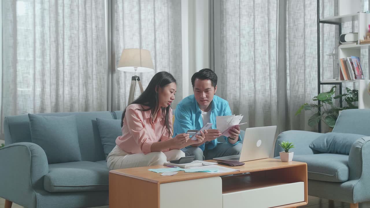 クレジットカードとスマートフォンを持ったラップトップを持ったアジア人カップルが,お金を支払うことができないため,頭痛を抱えています.