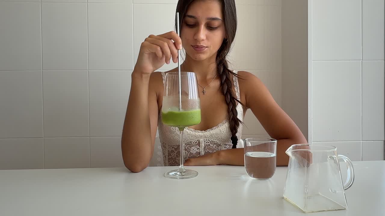 Giovane donna che versa il latte in una bevanda verde e mescola.