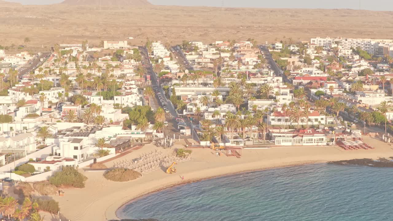 Dronebillede ved solopgang over Playa del Medio Beach Area i Fuerteventura, De Kanariske Øer, Spanien, der afslører en buet kystlinje, hvidkalket by og gyldent atlanterhavslys
