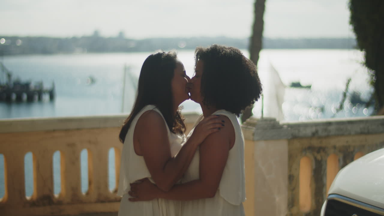 Vista laterale di spose felici che si abbracciano e si baciano sull'argine prima della cerimonia di matrimonio