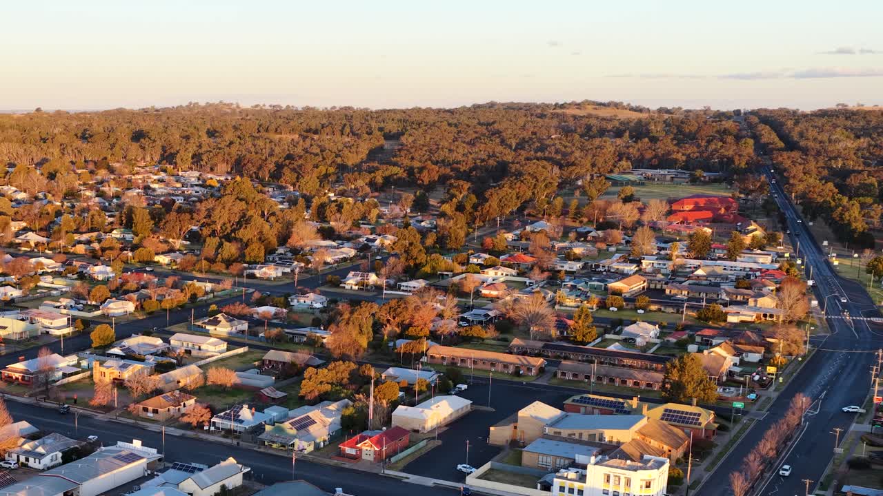 Drone camera glides above Coonabarabran’s main street at sunset, revealing small-town buildings, tree-lined roads, and golden hour lighting in rural New South Wales