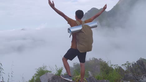 asian hiker male reaching up top of foggy mountain and raising his hands