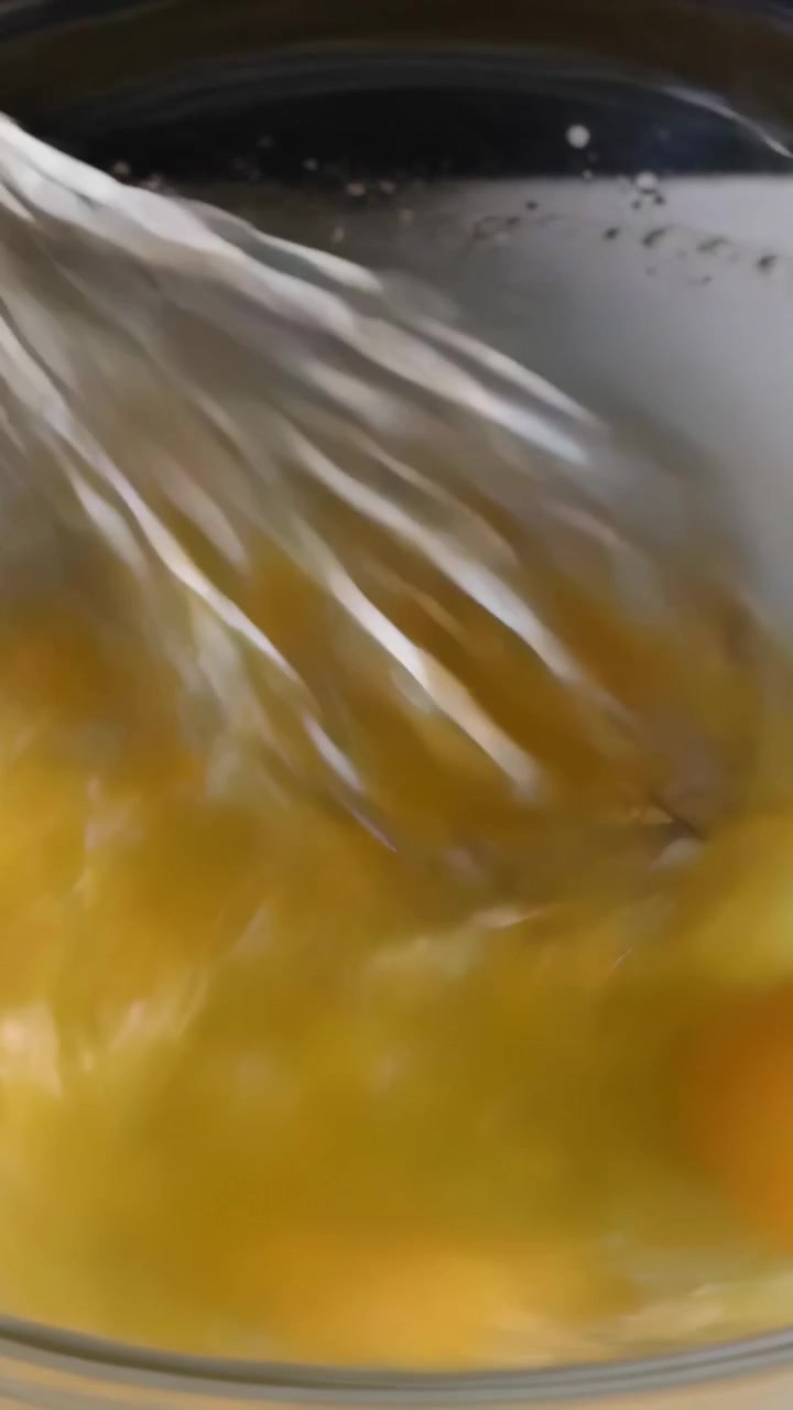 Video vertical: Batiendo tres huevos en un tazón de vidrio sobre la encimera, el batidor entrando y mezclando para cocinar.