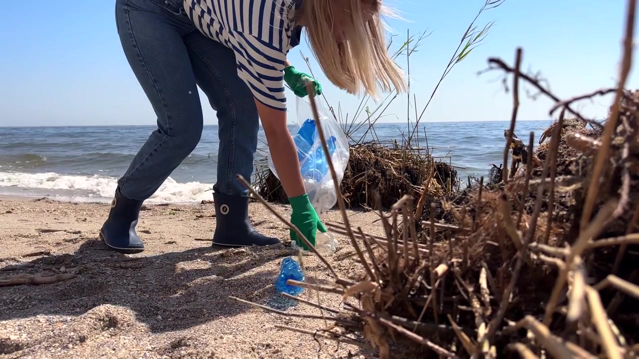 Kvinde rydder plastikaffald fra sandstrand