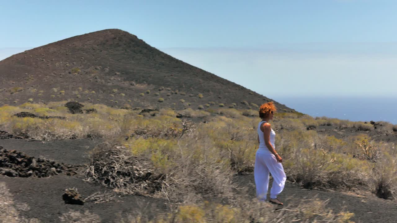 An elegant woman in white walking around in a volcanic islans, with a sea of clouds in the background