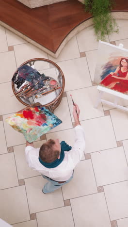 artista baila por retrato de mujer en el estudio. pintor alegre con paleta y pincel se da la vuelta mientras trabaja en la galería. diseñador con inspiración creativa