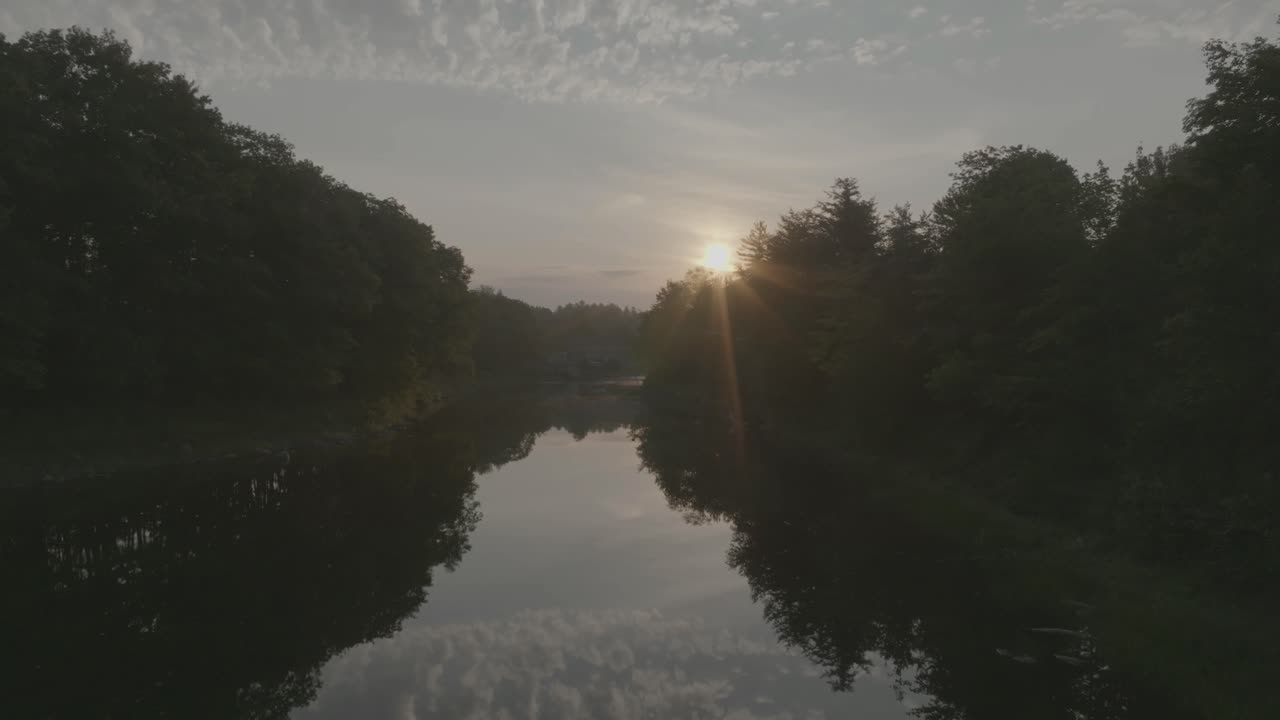 volando sobre un río todavía reflectante dentro de la naturaleza durante la puesta de sol