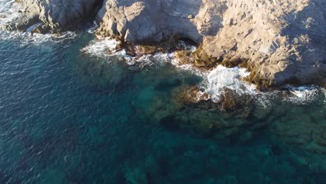 Impresionante-Vista-Aérea-De-Arriba-Hacia-Abajo-De-Las-Olas-Azules-Que-Se-Estrellan-Contra-Las-Rocas,-Descenso-Lento,-Día