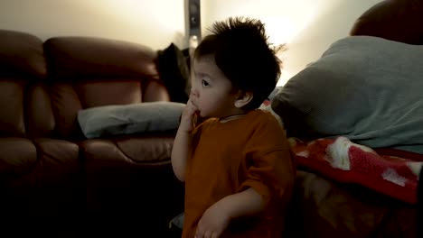 an 18-month-old baby boy watches tv in the evening, captivated by the screen and sucking his fingers