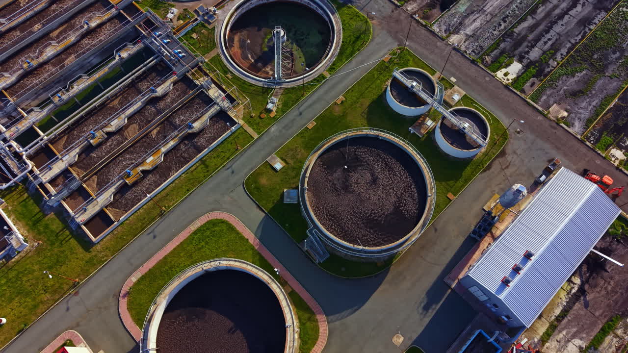 View of a wastewater treatment facility showing several tanks and processing areas during daylight in an urban setting