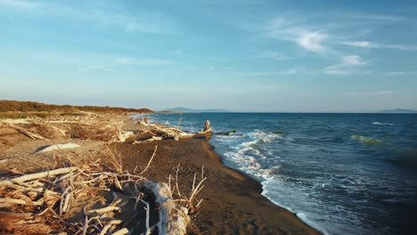 aerial drone footage flying toward a sandy sunset beach at the seaside near castiglione in the iconic maremma nature park in tuscany, italy, with waves, islands and a cinematic dramatic red sky