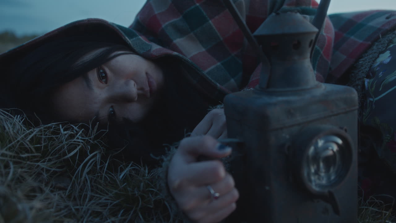 Introspective Woman Lying on Grass and Gazing at Lantern in Twilight