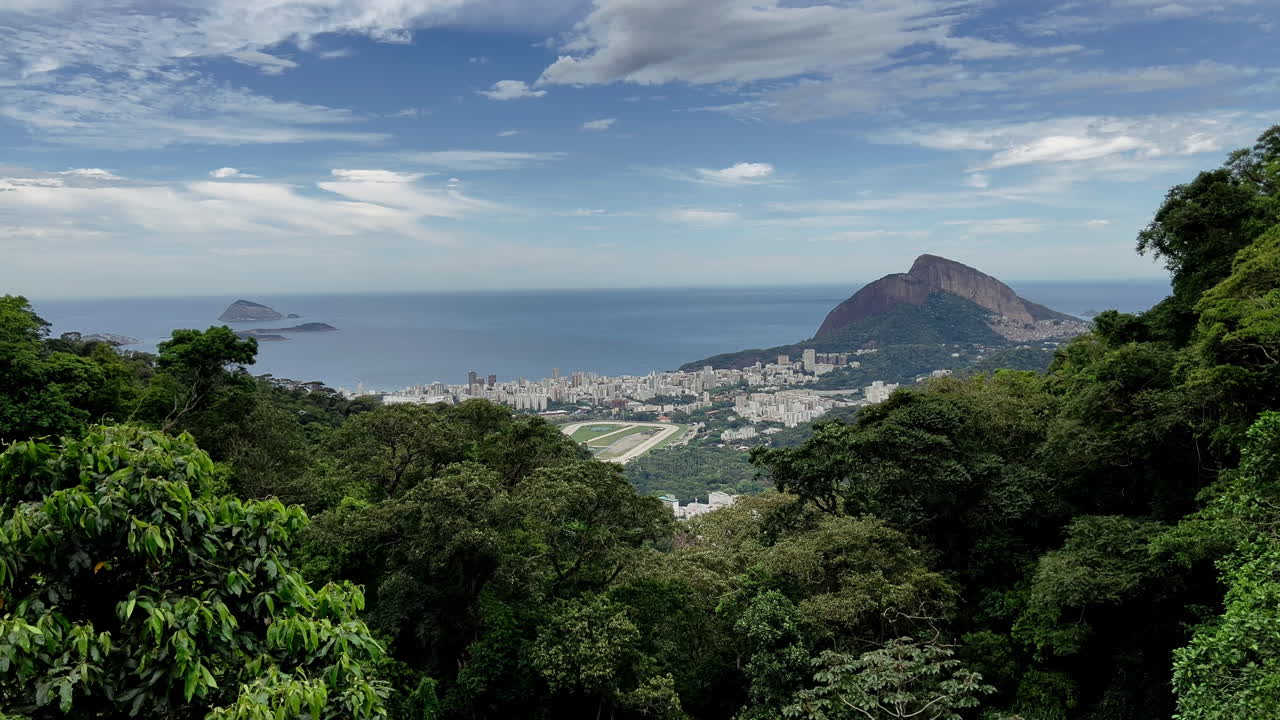 Un’ampia inquadratura mozzafiato delle lussureggianti colline di Rio, che cattura la silhouette dell'iconica montagna Dois Irmãos e l'ippodromo Jockey Club immerso nel denso paesaggio urbano
