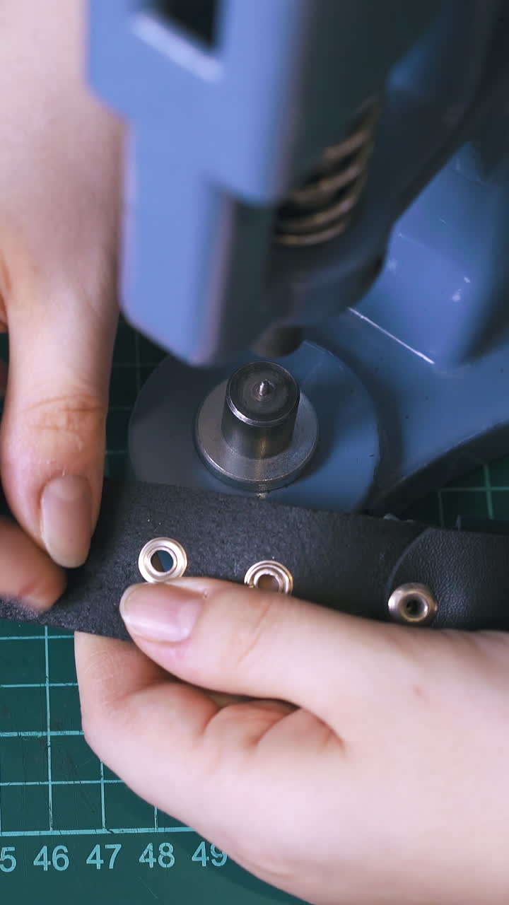 CU: Skilled woman worker fixes silver eyelets in fashionable leather belt holes with press machine close view