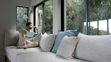 thoughtful biracial man sitting on sofa at home, slow motion, copy space