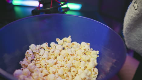 close up of popcorn in blue bowl with person beside it, colorful blinking light reflecting off surfaces, condenser microphone partially visible above bowl