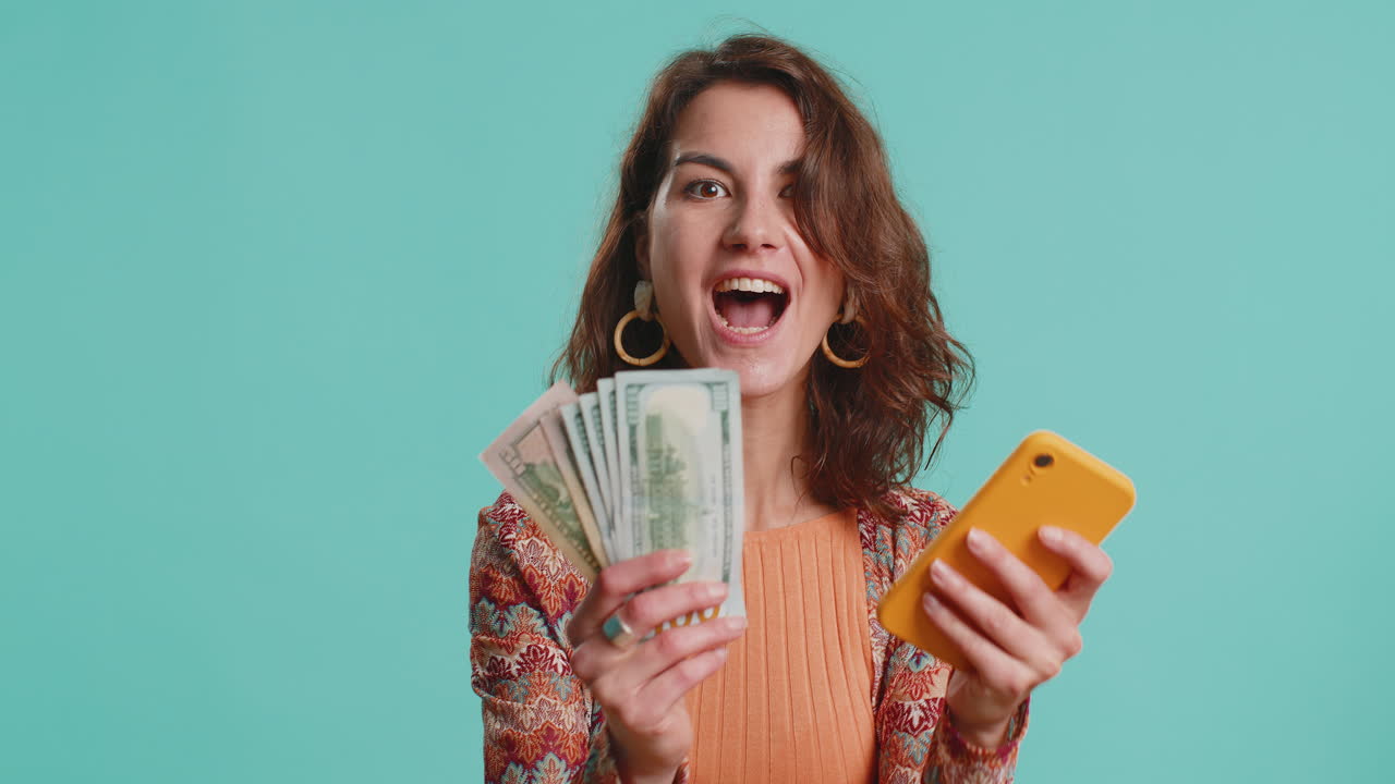 Young woman use smartphone rejoicing win receiving money dollar cash banknotes celebrating success