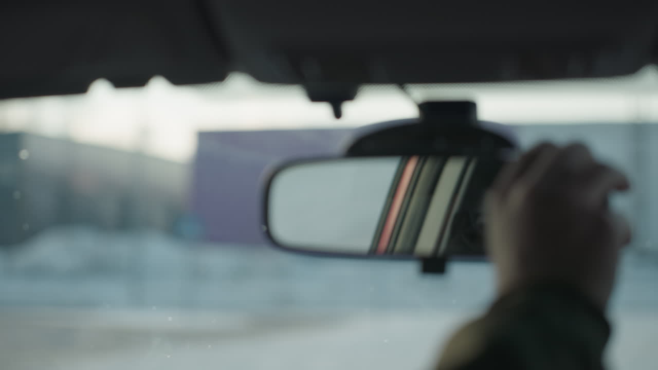 rear view mirror reflecting young boy wearing eyeglasses as he adjusts mirror inside vehicle with soft focus winter background seen through windshield and light glare on glass
