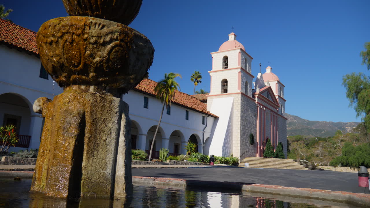 el edificio histórico de la misión de santa bárbara con una fuente en primer plano que refleja la arquitectura católica española