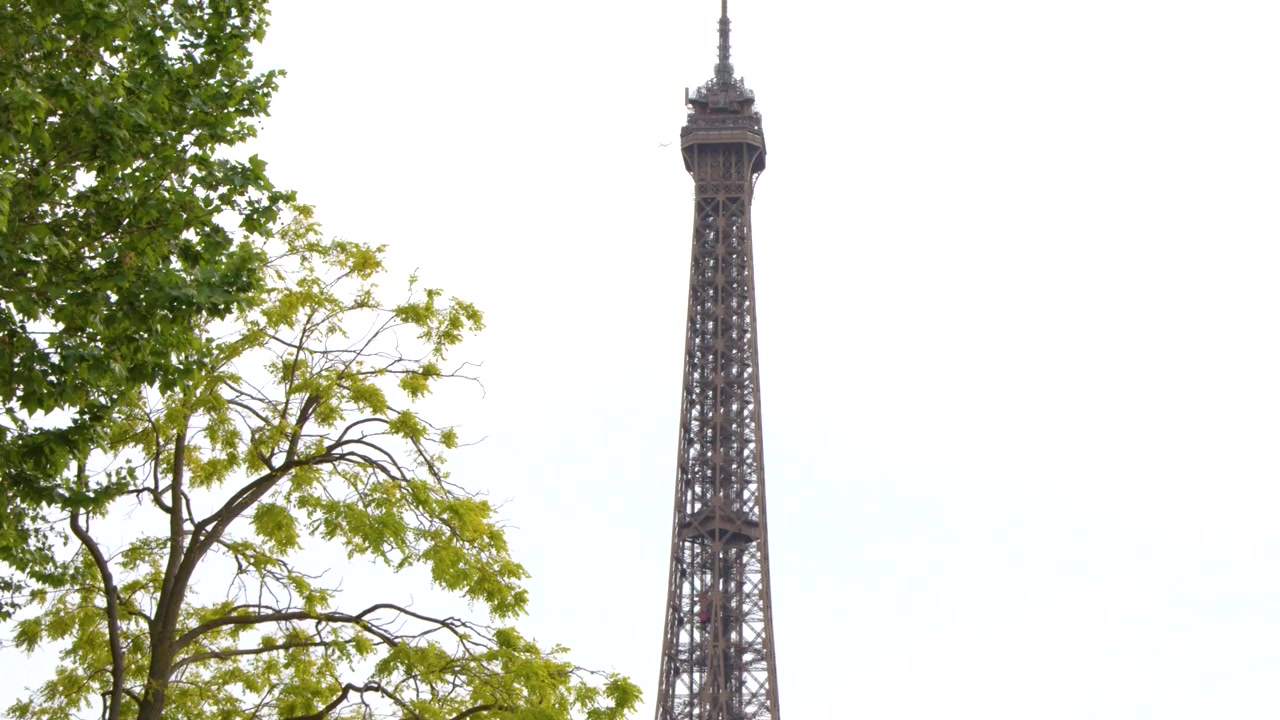 Una ripresa verticale in tilt rivela l'iconica torre a traliccio di ferro contro un cielo coperto.