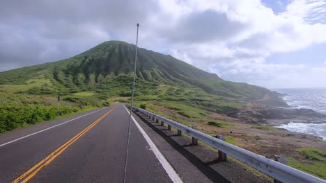 driving at coastline road with lots of green vegetation and volcanic hill in front