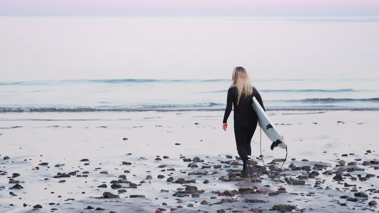 바다로 걸어가는 서프보드를 들고 있는 웨이트슈트를 입은 여성의 뒷면