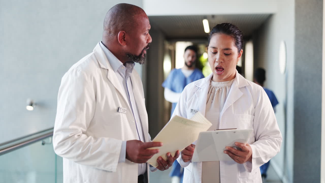 Due medici di diversa origine che discutono cartelle cliniche nel corridoio dell'ospedale.