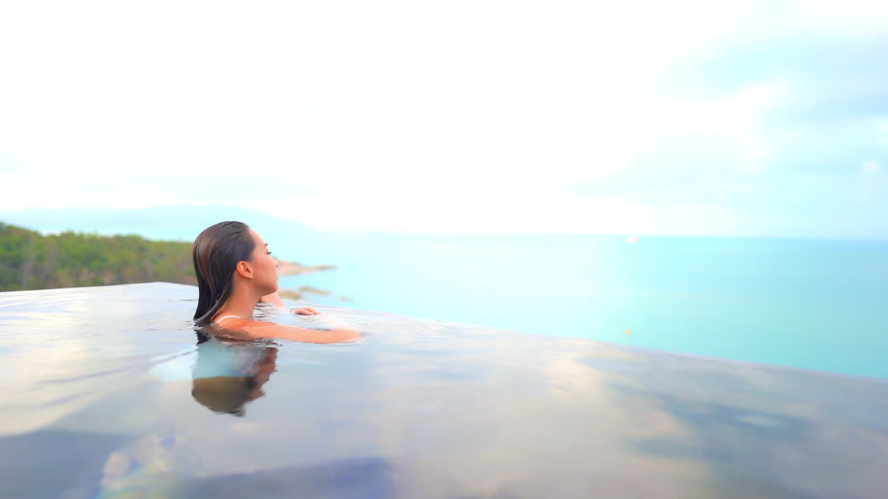 수영을 마친 한 여성이 수영장 물가에 접근하여 바다와 섬 가장자리의 탁 트인 전망을 제공합니다.