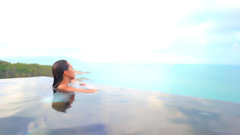 a woman fresh from swimming approaches the water edge of the pool giving her the panoramic view of the ocean and island edge