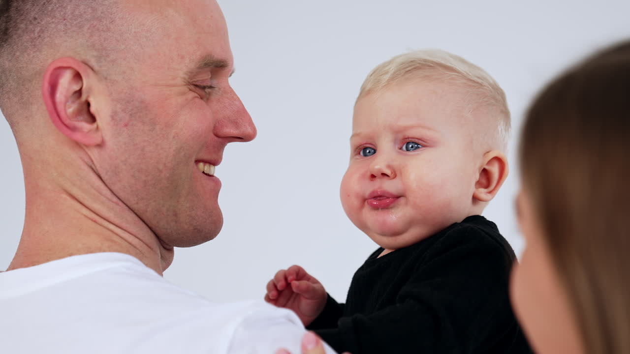 Father is holding his cute blond baby boy. Little kid cries and makes faces and dad repeats after him. Close up.