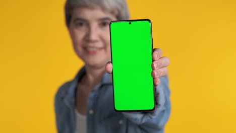 mujer asiática de mediana edad mostrando un teléfono inteligente con pantalla verde
