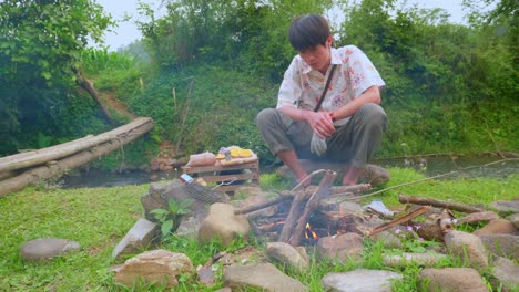 asian young man preparing bonfire for a barbecue in middle of river meadow