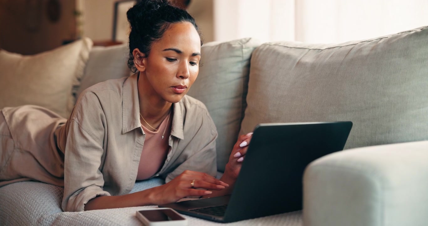 Young Woman Working on Laptop While Relaxing on Sofa