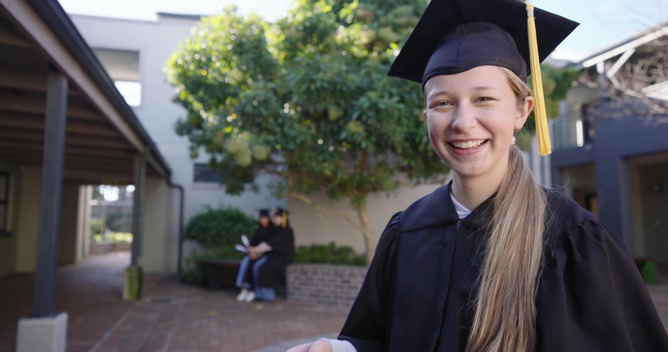 Absolventky v promočních talárech drží srolované diplomy, smějí se a jásají, když se blíží kamera.