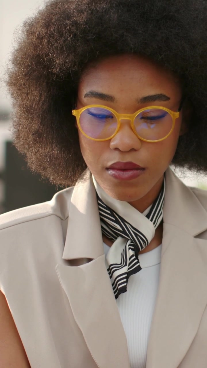 Vertical video: Looking down African woman reading phone at work, wearing yellow glasses