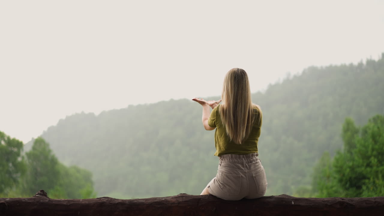 mujer con el cabello suelto alcanza las manos para atrapar gotas de lluvia pasar tiempo en el complejo ecológico de las tierras altas en
