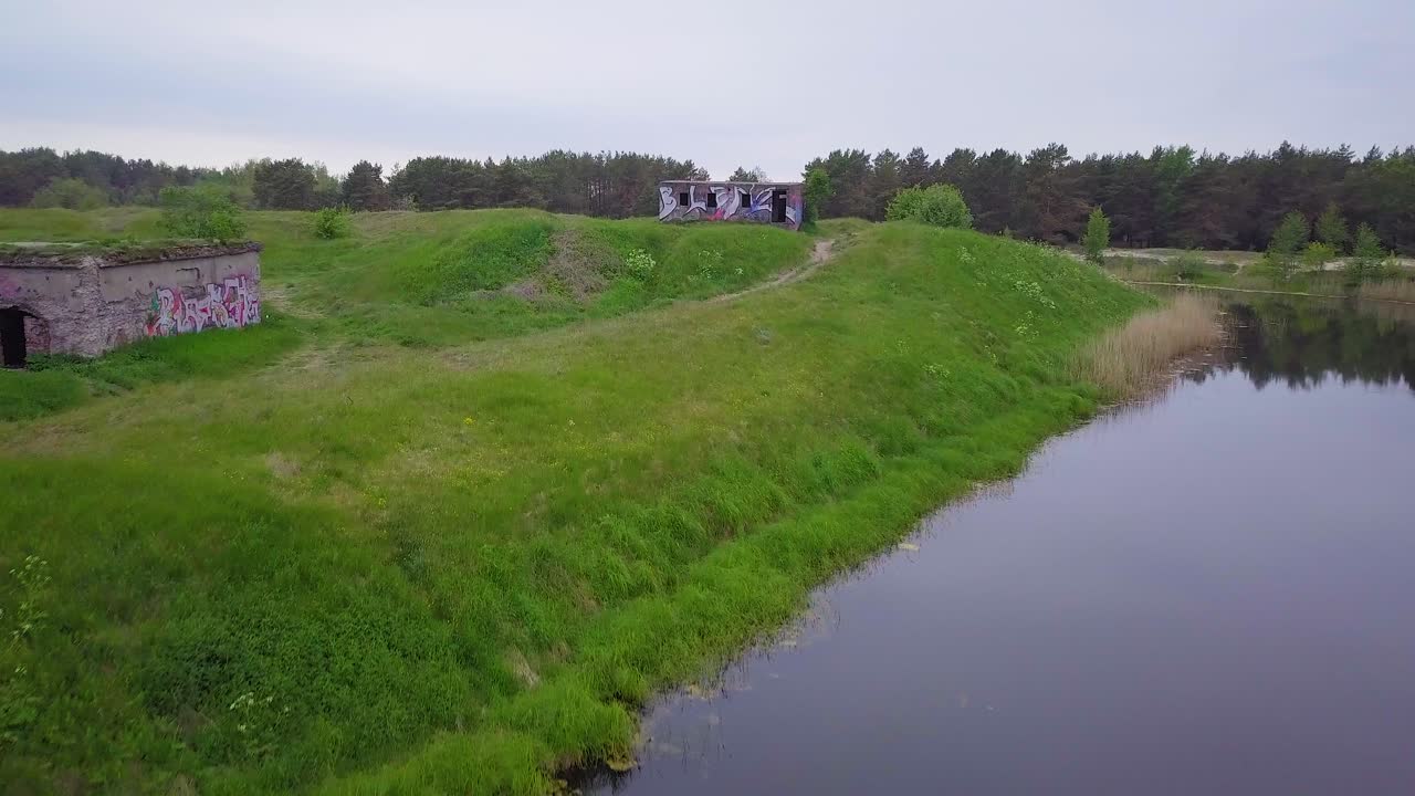 Aerial view of abandoned concrete seaside fortification building, Southern Forts near the beach of Baltic sea in Liepaja at overcast summer day, wide ascending drone shot moving forward over the water