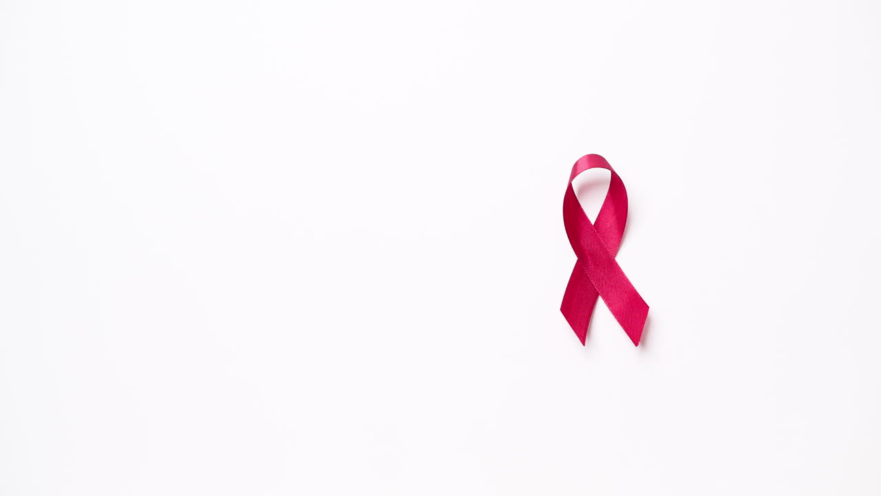 Détail d'une main d'homme attachant un ruban rouge sur fond blanc