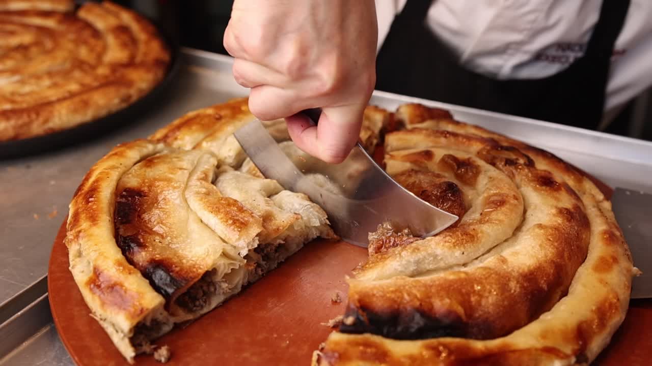 Primo piano di una mano che taglia un burek appena sfornato.