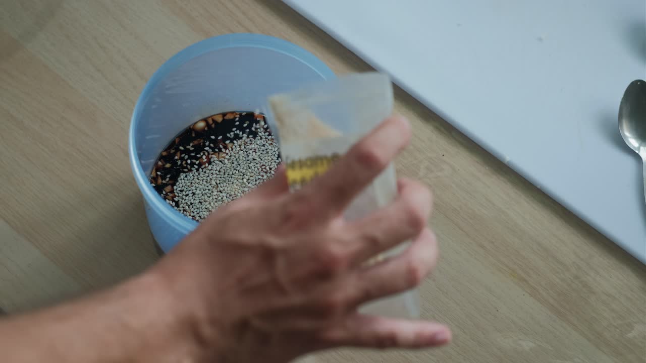 Pouring white sesame seeds into a plastic container of soy sauce marinade. -closeup shot