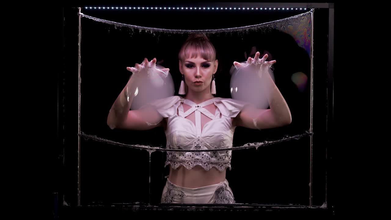 una joven hace trucos con burbujas de jabón. toma dos burbujas grandes con sus manos.