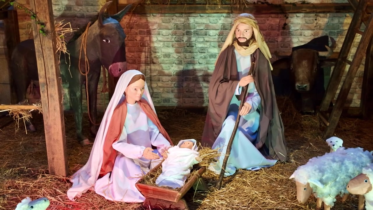 Close-up de um presépio de Natal tradicional apresentando figuras de Maria, José e o Menino Jesus em uma manjedoura, cercado por um burro, boi e ovelhas dentro de um estábulo decorado com palha