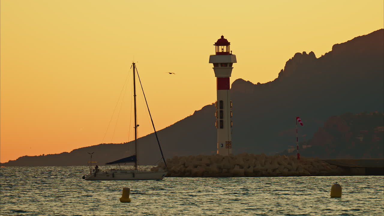 Boat moving on the sea near a lighthouse with the mountains on the background at sunset in Cannes, France