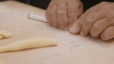 close up slow motion footage of old weathered hands cutting a roll of dough to make pasta shells