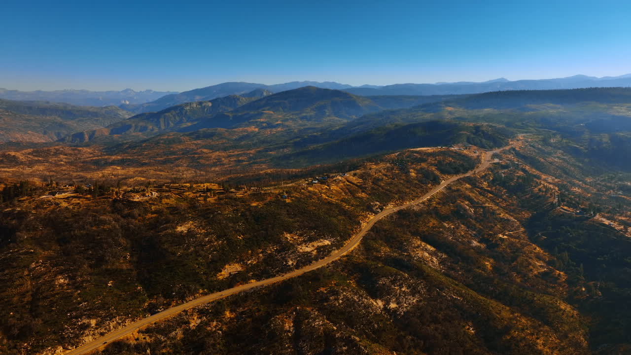 Highway going along the mountain with some buildings on top. View of Sierra National Forest in USA from aerial perspective.