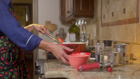 woman pours onion in to red pan while cooking at the stove