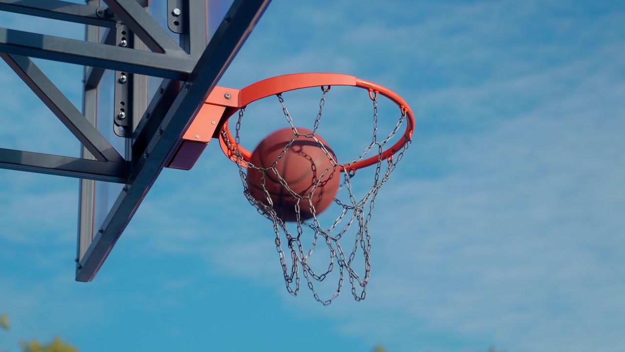 Palla da basket al rallentatore che entra nel canestro contro un cielo blu.